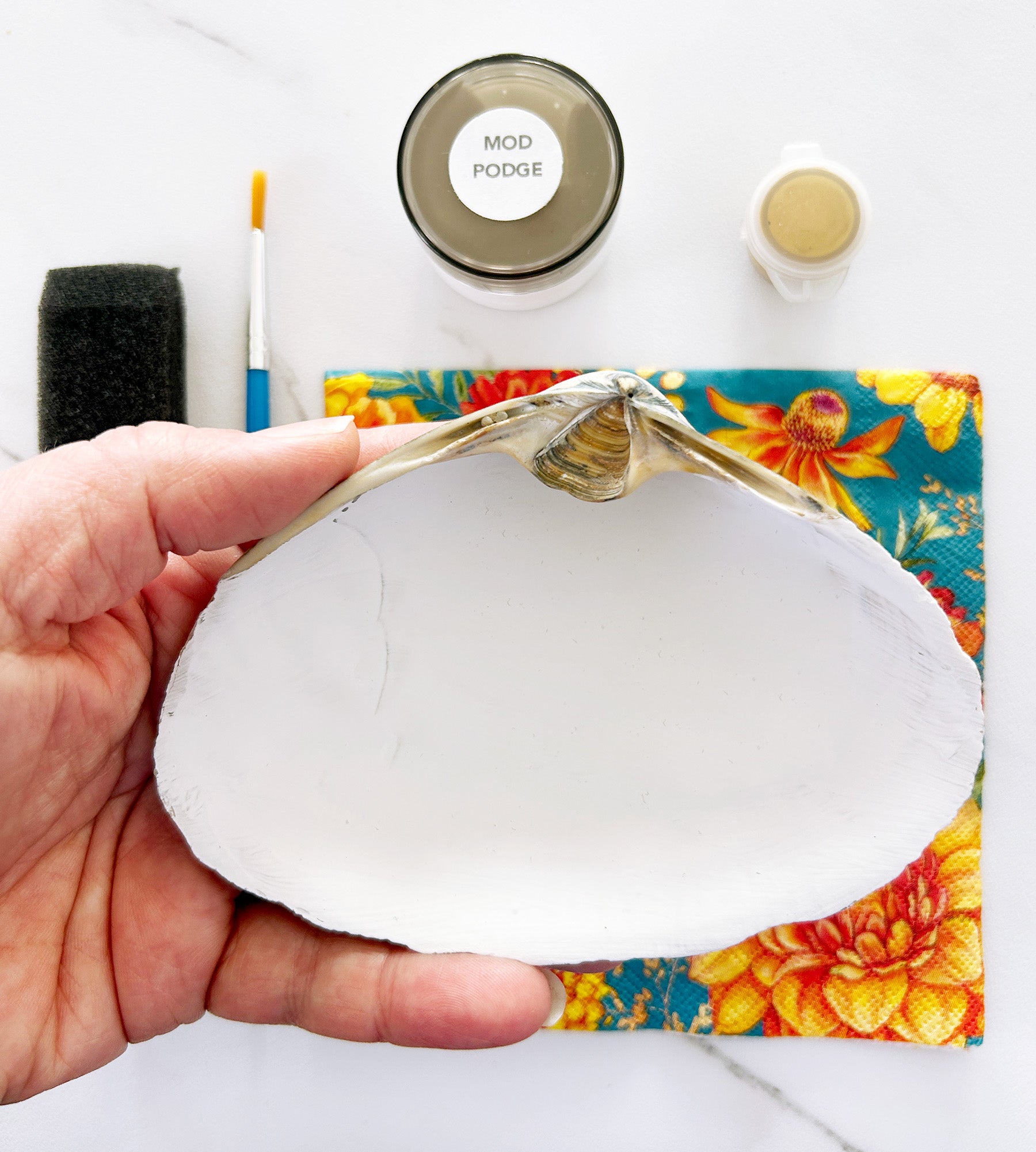 Hand holding a white shell with gold accents on a colorful floral background