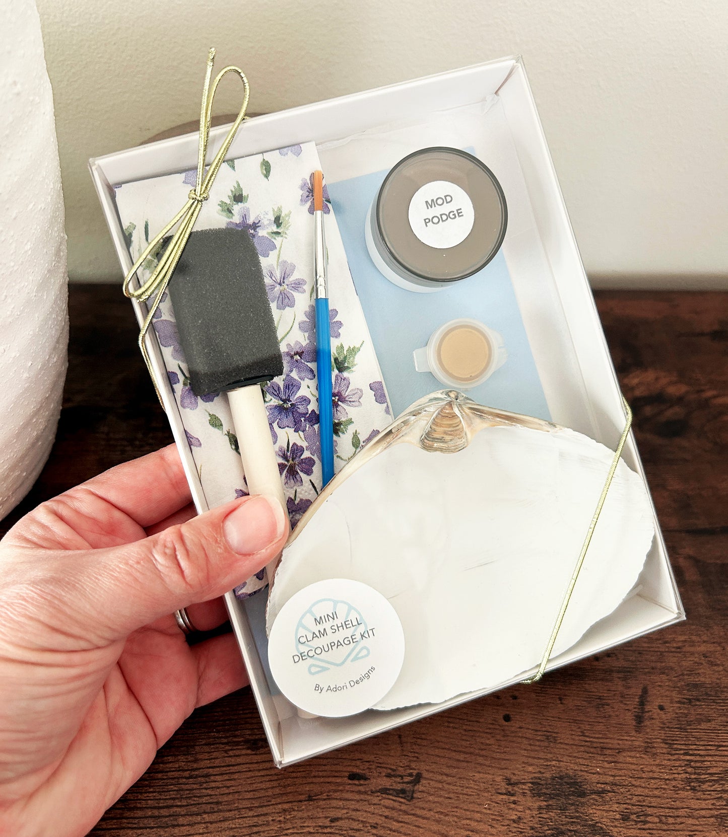 Decoupage kit with tools and craft supplies held by a hand, displayed on a wooden surface.