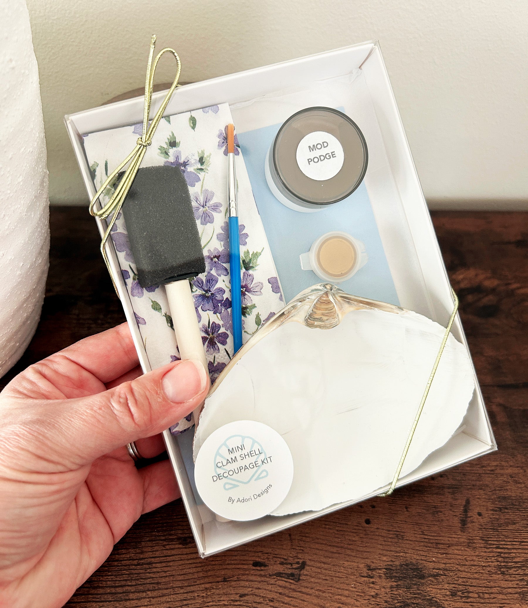 Decoupage kit with tools and craft supplies held by a hand, displayed on a wooden surface.