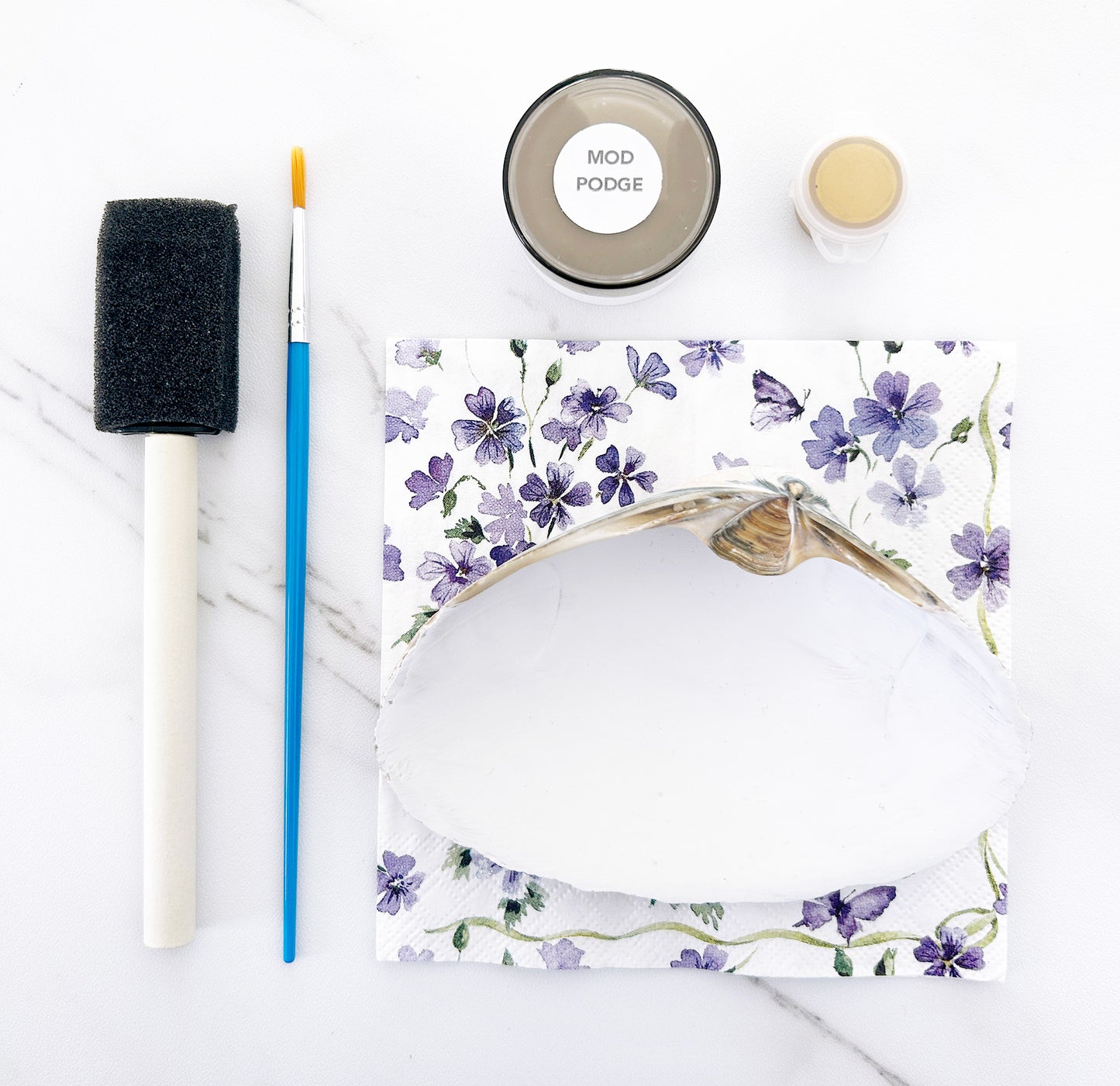 White seashell with floral design, foam brush, and Mod Podge on a white background