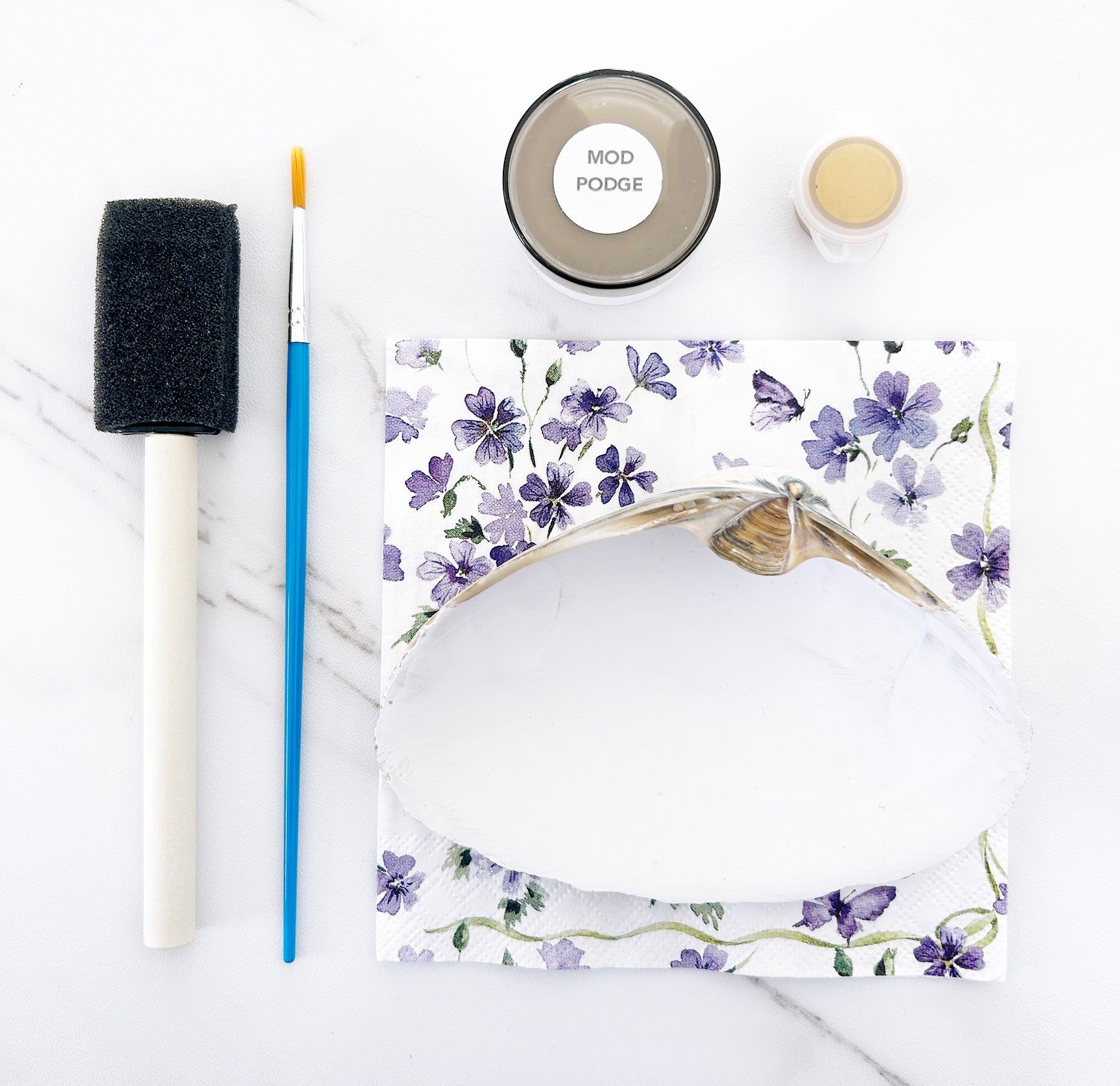 White seashell with floral design, foam brush, and Mod Podge on a white background